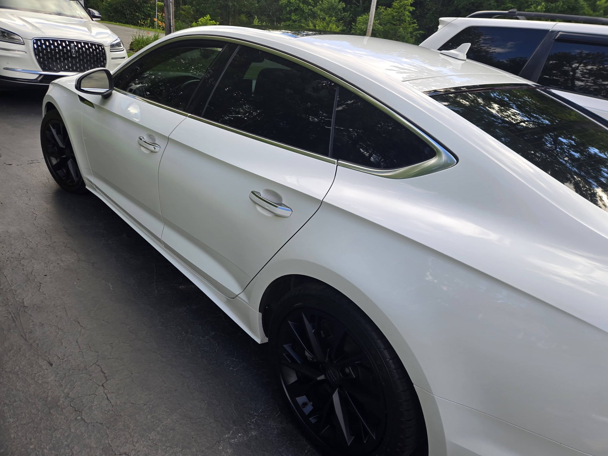 Side profile of a white Audi A5 reflecting the trees around it
